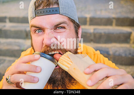 Se libérer de la faim et de la soif. Homme barbu ayant hot-dog et le café pour pause gourmande. Portrait guy profiter de la restauration rapide et de boisson chaude pour pause repas. Hipster snacking sur des escaliers pendant de repos. Banque D'Images