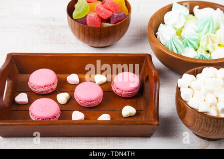 Macarons fraises, confiture, les meringues et les guimauves dans bols et un plateau sur un fond de bois. Banque D'Images