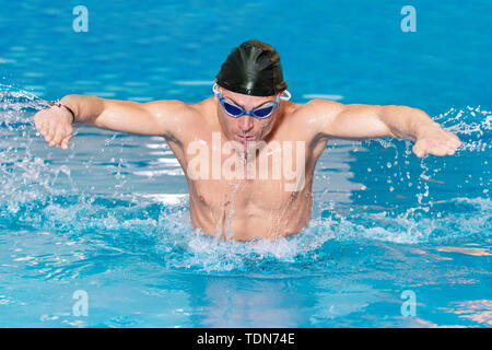 Nageur musculaire young man in black cap dans la piscine, l'exécution de papillon . Banque D'Images