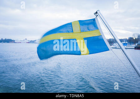 Drapeau national suédois qui oscille au vent à l'arrière d'un ferry naviguant dans l'archipel de Stockholm sous un ciel couvert d'hiver. Banque D'Images