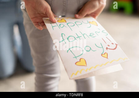 Close-up of méconnaissable girl holding creative fête des pères carte avec coeurs derrière retour tout en se préparant à célébrer le père bien-aimé Banque D'Images