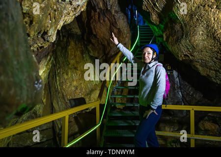 Jeune femme avec casque pointe vers les escaliers en Ialomita grotte, montagnes de Bucegi. Une grotte dans les montagnes de Bucegi, Carpates, Roumanie Banque D'Images