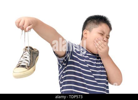 Dégoûté gros garçon tenant une paire de chaussures stinky malodorantes et isolé sur fond blanc, Banque D'Images