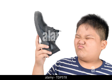 Dégoûté gros garçon tenant une paire de chaussures en cuir stinky malodorantes et isolé sur fond blanc, le concept de soins de santé Banque D'Images