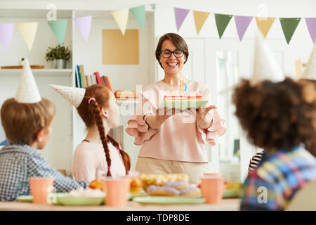 Portrait de mère heureuse ce qui porte le gâteau d'anniversaire avec des bougies pour des enfants parti, copy space Banque D'Images