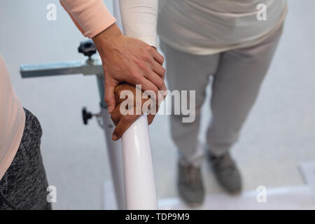 Physiothérapeute femelle helping patient à pied avec les barres parallèles Banque D'Images