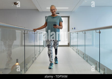 Mobilité female patient avec prothèse à l'aide de téléphone mobile tout en marchant dans le couloir Banque D'Images