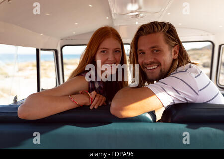 Happy young couple looking at camera sur le siège avant de camper van at beach Banque D'Images