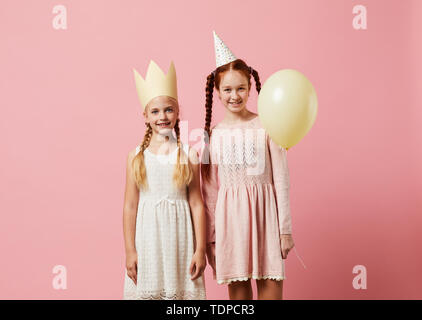 Portrait de deux jeunes filles wearing party hats posant contre fond rose, copy space Banque D'Images