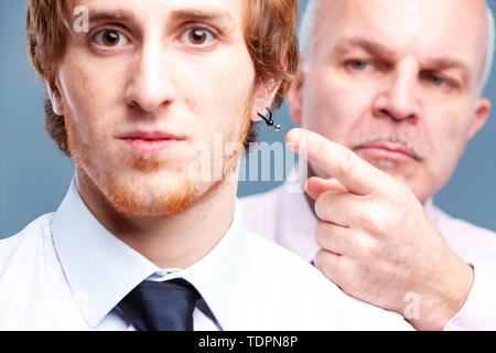 Parti conservateur senior businessman, patron ou manager pointant vers d'oreille porté par un employé plus jeune qui regarde la caméra dans de grands yeux trepidati Banque D'Images