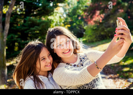 Deux sœurs en prenant un auto-portrait d'eux-mêmes au cours d'une sortie en famille dans un parc de la ville sur une chaude journée d'automne : Edmonton, Alberta, Canada Banque D'Images