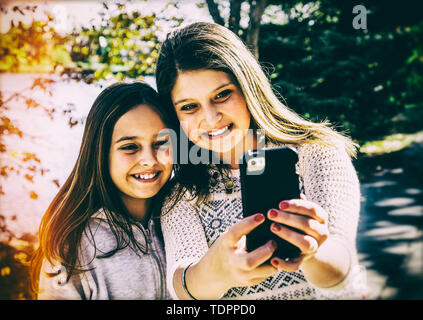 Deux sœurs en prenant un auto-portrait d'eux-mêmes au cours d'une sortie en famille dans un parc de la ville sur une chaude journée d'automne : Edmonton, Alberta, Canada Banque D'Images