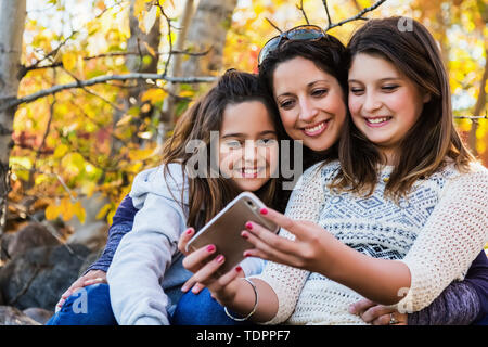 Une maman et ses deux filles en prenant un auto-portrait au repos pendant une sortie en famille dans un parc de la ville sur une chaude journée d'automne ; Edmonton, Alberta, Canada Banque D'Images