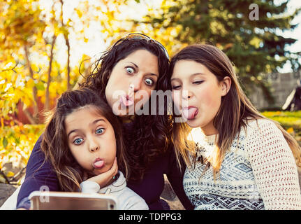 Une maman et ses deux filles en prenant un auto-portrait au repos pendant une sortie en famille dans un parc de la ville sur une chaude journée d'automne ; Edmonton, Alberta, Canada Banque D'Images