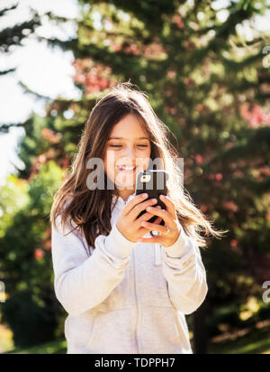 Une jeune fille de sms sur un téléphone intelligent tout en prenant une marche dans un parc de la ville pendant un jour d'automne chaud et ensoleillé ; Edmonton, Alberta, Canada Banque D'Images