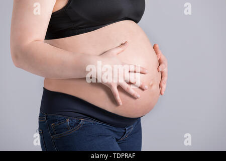 Une jeune femme enceinte tenant son ventre dans un studio sur fond clair ; Edmonton, Alberta, Canada Banque D'Images