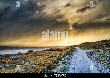 Chemin couvert de neige le long de la côte d'or avec la lumière du soleil éclairant les nuages ; à South Shields, Tyne and Wear, England Banque D'Images