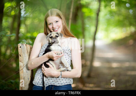 Chien domestique (Canis lupus f. familiaris), jeune femme tenant un mignon Puggle sur bras, Allemagne Banque D'Images