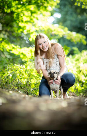 Chien domestique (Canis lupus f. familiaris), bonne à la jeune femme avec un Puggle, coup de genou sur le sol forestier, Allemagne Banque D'Images