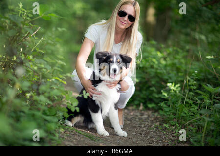 Berger Australien (Canis lupus f. familiaris), mettent bas avec une jeune femme sur un chemin forestier, Allemagne Banque D'Images