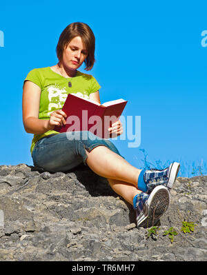 Jeune fille assise sur un rocher et la lecture d'un livre, Allemagne Banque D'Images