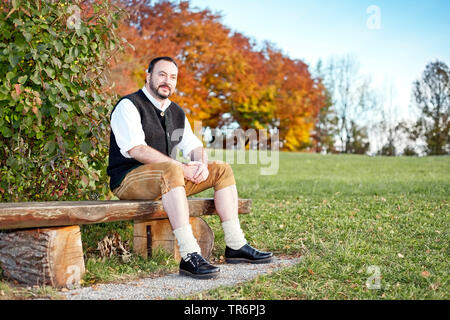 L'homme en costume traditionnel bavarois assis sur un banc en automne, l'Allemagne, la Bavière Banque D'Images