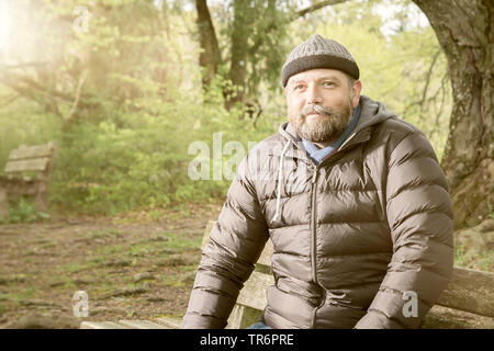 Homme avec barbe et wooly hat assis sur un banc dans la nature, Allemagne Banque D'Images