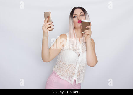 Image de jolie belle jeune femme blonde en chemise blanche posant sur fond blanc à boire du café et à l'aide de son shartphone Banque D'Images