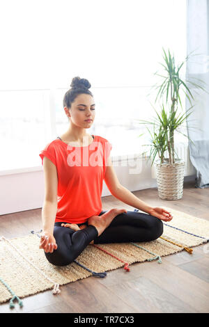 Jolie jeune femme brune de l'exercice et assis en position du lotus yoga tout en se reposant à la maison Banque D'Images