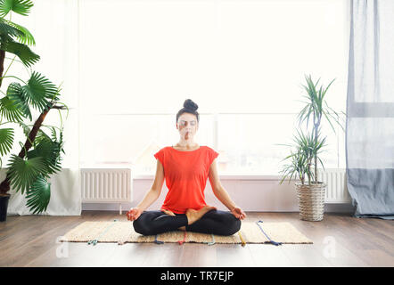 Jolie jeune femme brune de l'exercice et assis en position du lotus yoga tout en se reposant à la maison Banque D'Images