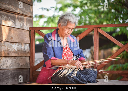 La vie Asie vieille femme travaillant dans accueil / Grand-mère vivant à la campagne sérieuse de la vie des populations rurales dans la Thaïlande weave panier de bambou artisanat sur wo Banque D'Images