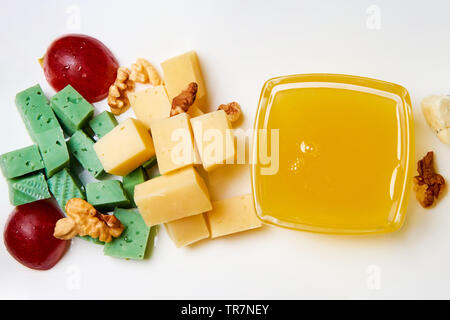 Fromage en tranches avec les noix, les raisins et le miel sur une plaque blanche. Banque D'Images