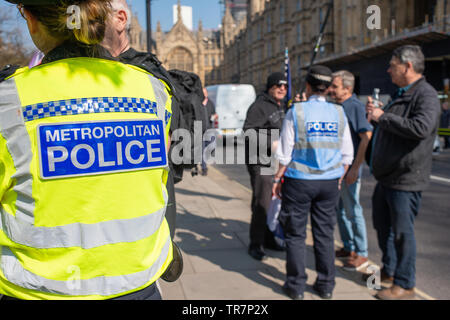 Officier de police au premier plan, montre en tant qu'officier de liaison de police traite avec quelques manifestants au mois de mars pour quitter le rallye dans le centre de Londres. Banque D'Images