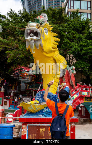 Un homme jette de l'argent dans la bouche du poisson pour la bonne chance, Kwun Yam culte, Repulse Bay, Hong Kong, Chine Banque D'Images