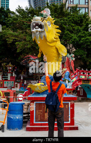 Un homme jette de l'argent dans la bouche du poisson pour la bonne chance, Kwun Yam culte, Repulse Bay, Hong Kong, Chine Banque D'Images