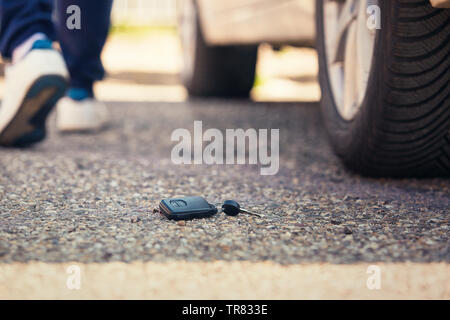 Clé de voiture tombent sur la route asphaltée. Conducteur a perdu la clé du véhicule et s'éloigne. Concept L'infortune. Banque D'Images