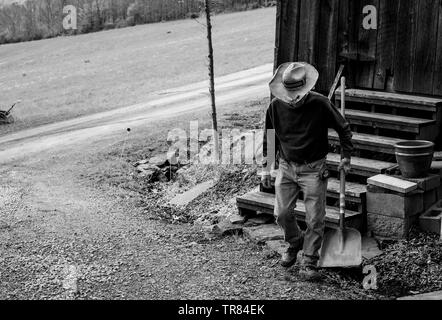 Un homme portant un chapeau de paille et transportant une pelle s'éloigne d'un vieux grainery. Banque D'Images