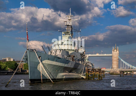Le HMS Belfast attraction touristique de bateau, amarré sur la Tamise en fin d'après-midi au soleil, avec le Tower Bridge et London Red Bus traversant Londres SE1 Banque D'Images