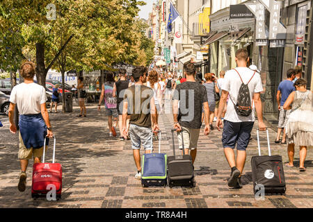 PRAGUE, RÉPUBLIQUE TCHÈQUE - Juillet 2018 : Groupe de visiteurs à roues traction valises à travers le centre-ville de Prague. Banque D'Images