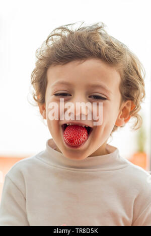 L'enfance et de l'alimentation saine concept. Enfant de mordre une fraise avec expression souriante. Banque D'Images