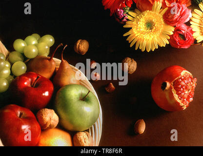 Still Life de panier avec différents fruits et fleurs sur fond sombre dans l'appartement d'angle de laïcs. Banque D'Images