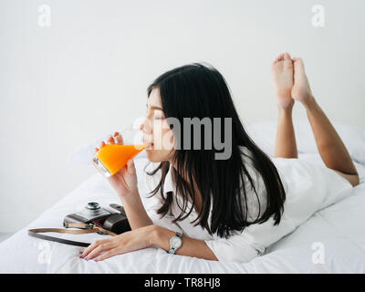 Asian woman boire un jus d'orange sur le lit chez lui, la notion de vie. Banque D'Images