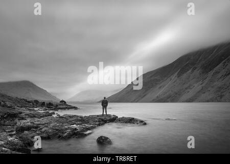 Lone figure en image paysage de l'eau as été au Royaume-Uni Lake District au cours de moody soirée de printemps en noir et blanc Banque D'Images