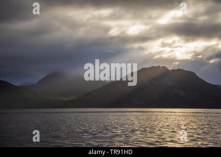 La lumière du matin et de l'humeur par le Romsdalsfjorden, la Norvège. Les rayons du soleil percent les nuages, tôt le matin, lumière chaude. Banque D'Images