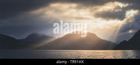 La lumière du matin et de l'humeur par le Romsdalsfjorden, la Norvège. Les rayons du soleil percent les nuages, tôt le matin, lumière chaude. Banque D'Images