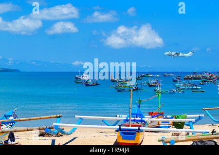 Bateaux de pêche colorés traditionnels dans le port du village de pêcheurs de Bali Jimbaran, Bali. Voir en mer horizon avec jet privé dans le ciel. Banque D'Images