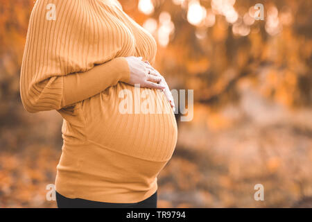 Pregnant woman wearing sweater jaune tricoté holding belly en plein air. La maternité. La maternité. 20s. Banque D'Images