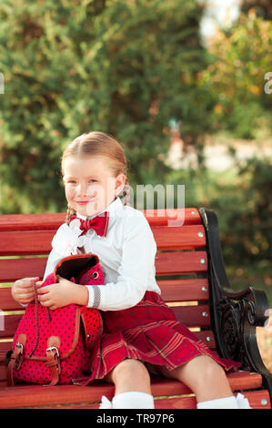 Cute girl enfant 6-7 ans vêtu de l'uniforme à l'extérieur. Smiling élève. À la recherche d'un appareil photo. L'enfance. Banque D'Images