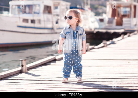 Baby Girl wearing denim élégant costume et la gaine à jetée en bois. La saison d'été. Enfant debout à l'extérieur. Banque D'Images