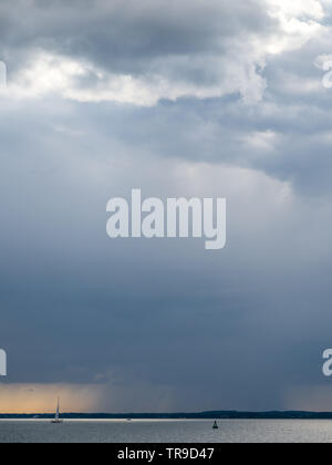 Un rainfront déménagement approchant sur Solent avec yacht unique solitaire en mer avec bouée sous big sky storm clouds coucher du soleil orange Banque D'Images